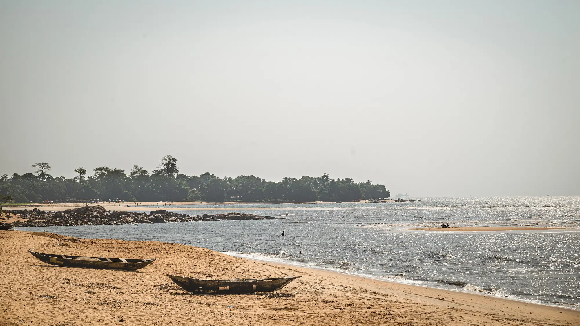 Wooden canoes on the sandy beach at Kribi, with a wooded headland across the water.