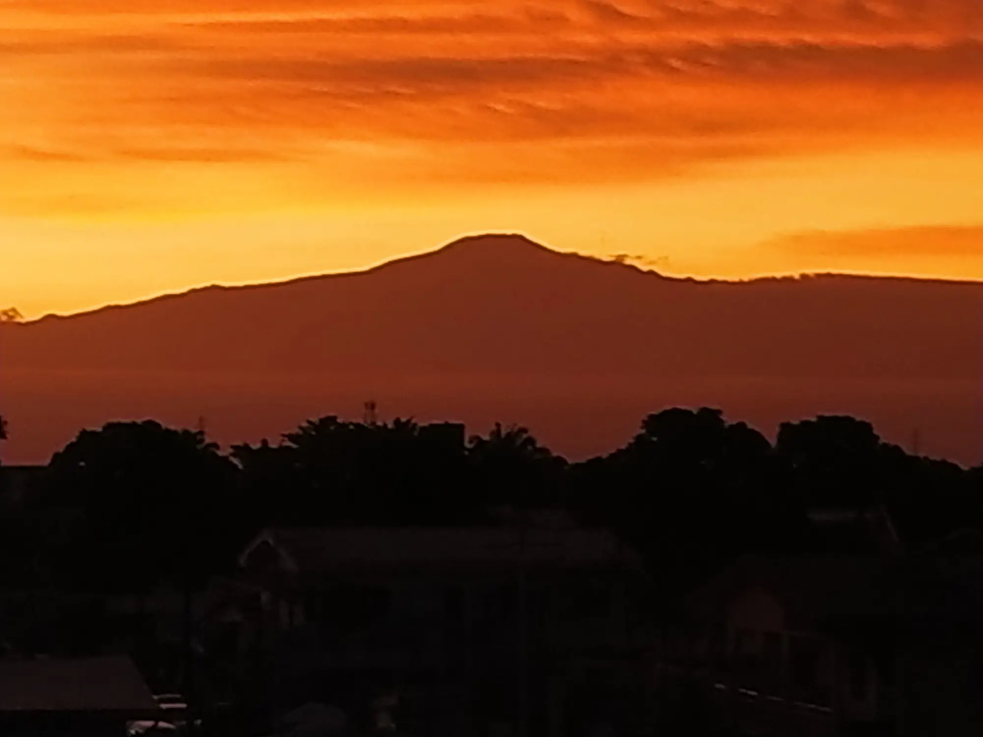 The silhouette of Mount Cameroon against an orange sky at sunset.