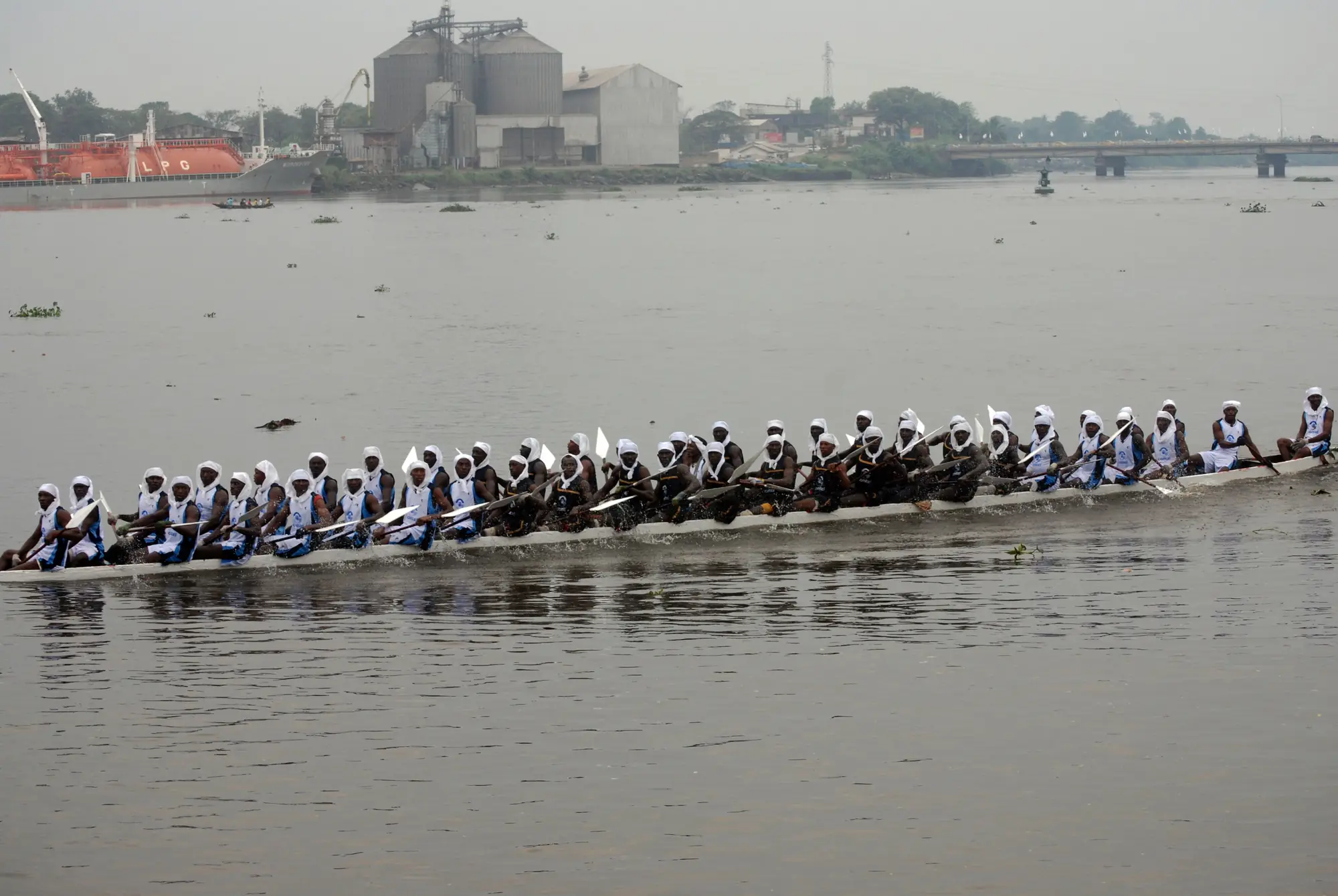 A long racing pirogue paddled by a crew in white on the Wouri river at Douala during the Ngondo.
